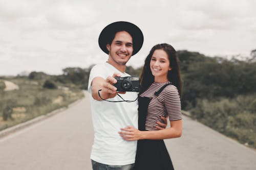 Happy young man and woman smiling and hugging while taking selfie on road during trip in countryside