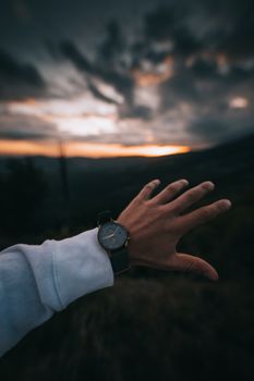 Crop faceless male tourist with wristwatch reaching hand toward picturesque view of sunset in countryside