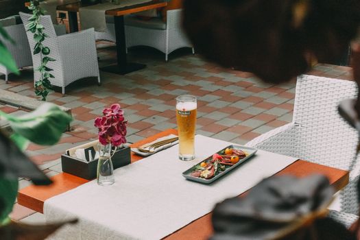 Charming outdoor cafe scene featuring a fresh salad and a glass of beer on a wooden table, adorned with vibrant pink flowers.