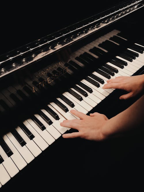 Unrecognizable skilled musician playing melody on keyboard of black piano while performing song during rehearsal in light room at home