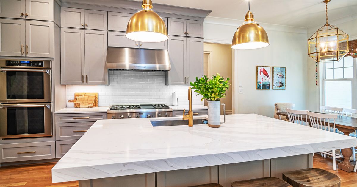 Grey kitchen cabinets with brass pendant lights and white marble island