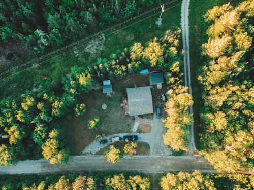 Free Overhead view of automobiles parked in yard of small house surrounded by tall green trees and long narrow roads in sunlight Stock Photo