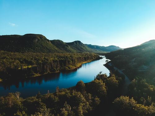 Free Light blue cloudless sky above mountain slopes and road between tall green trees in valley in sunlight Stock Photo