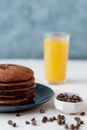Pile of yummy brown hotcakes on plate near spilled milk chocolate chips and glass of orange juice for breakfast