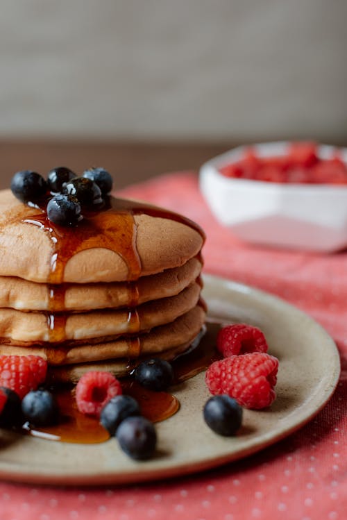Free Pile of appetizing golden pancakes with sweet syrup and whole ripe raspberries with blueberries on top Stock Photo