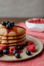 Pile of appetizing golden pancakes with sweet syrup and whole ripe raspberries with blueberries on top