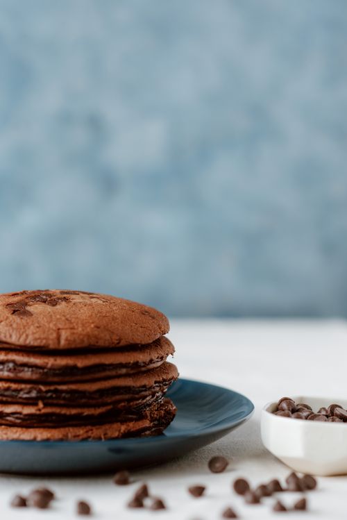 Free Pile of yummy brown hotcakes on plate near spilled chocolate chips for brunch on blurred background Stock Photo