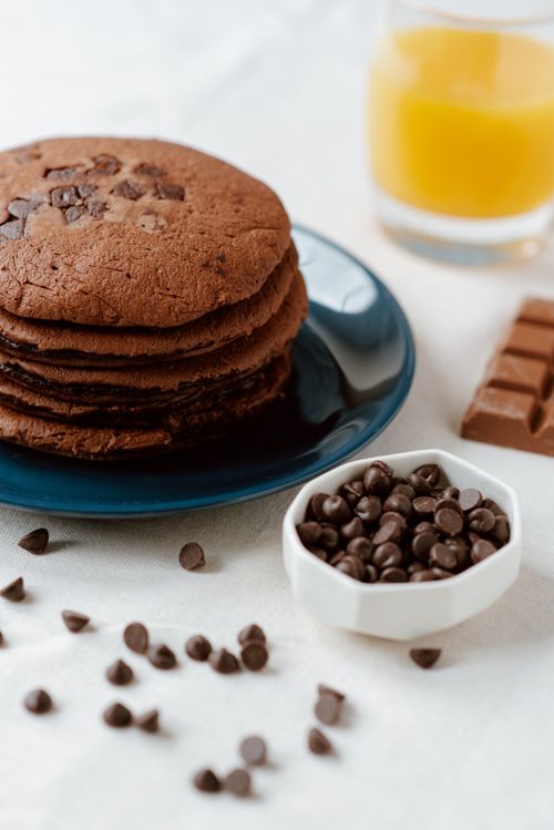Free From above of tasty brown pancakes with chocolate chips near glass of orange juice on table Stock Photo