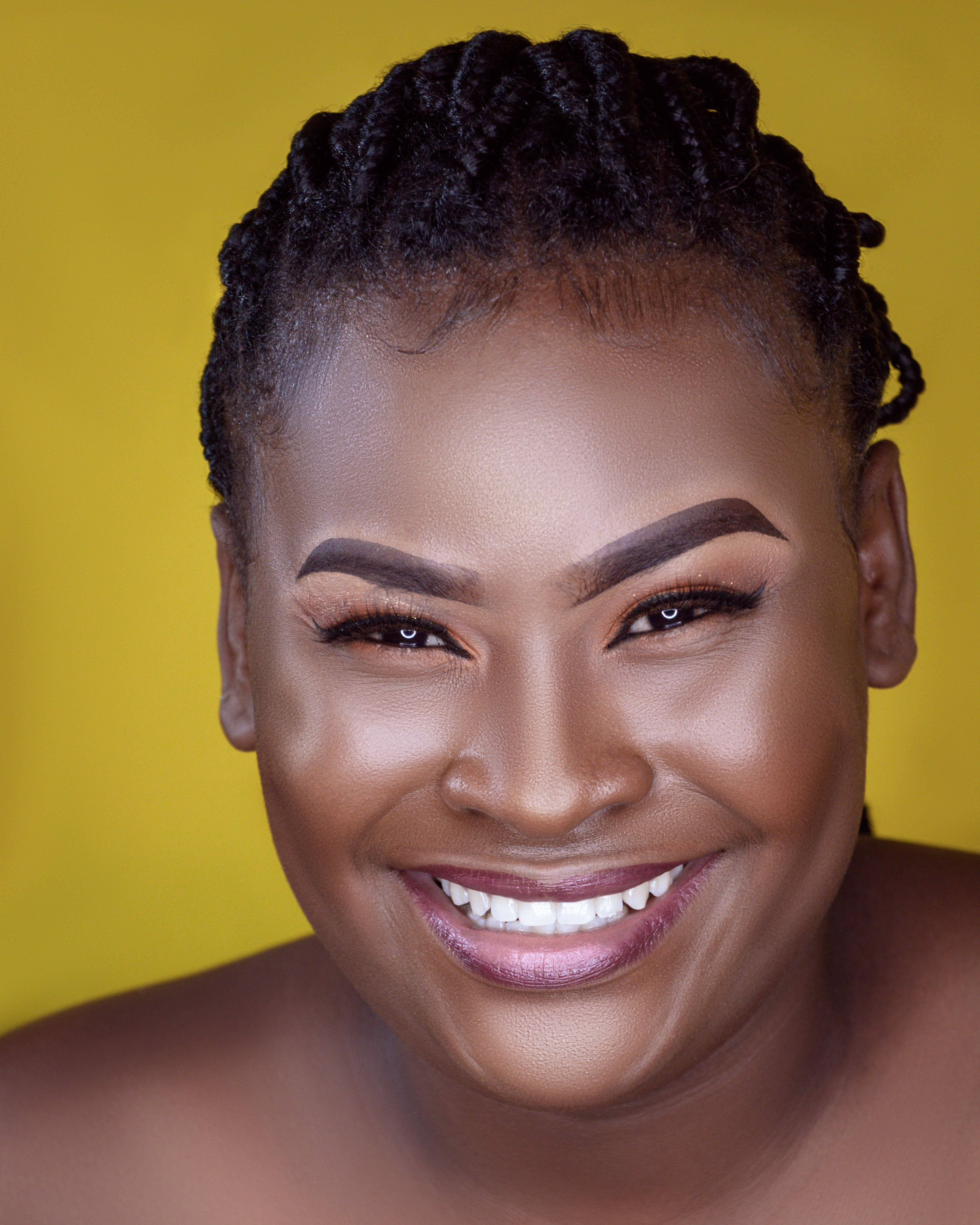 Close-up portrait of a smiling African American woman with afro hair against a yellow background.