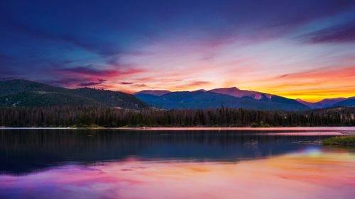 Free Stunning sunset over a peaceful lake with mountains and forests in the background. Stock Photo