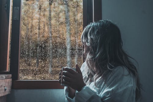 Woman in White Long Sleeve Shirt Looking out the Window