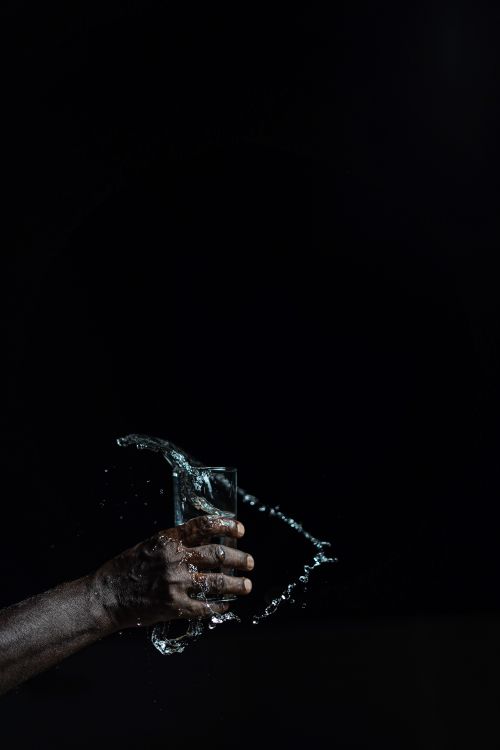 Free Hand holding a glass with water splashing against a black background in a dramatic capture. Stock Photo