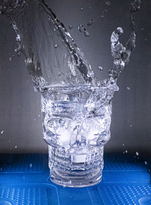 Free Crystal skull glass with water splash on blue surface. Stock Photo