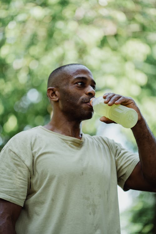 A Man in Crewneck T-shirt Drinking from a Plastic Bottle