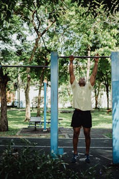 A man performs pull-ups in an outdoor park setting, showcasing fitness and strength.