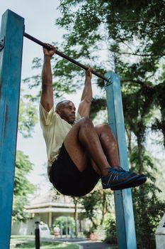 Athletic man hanging on pull-up bar, demonstrating strength and fitness outdoors.