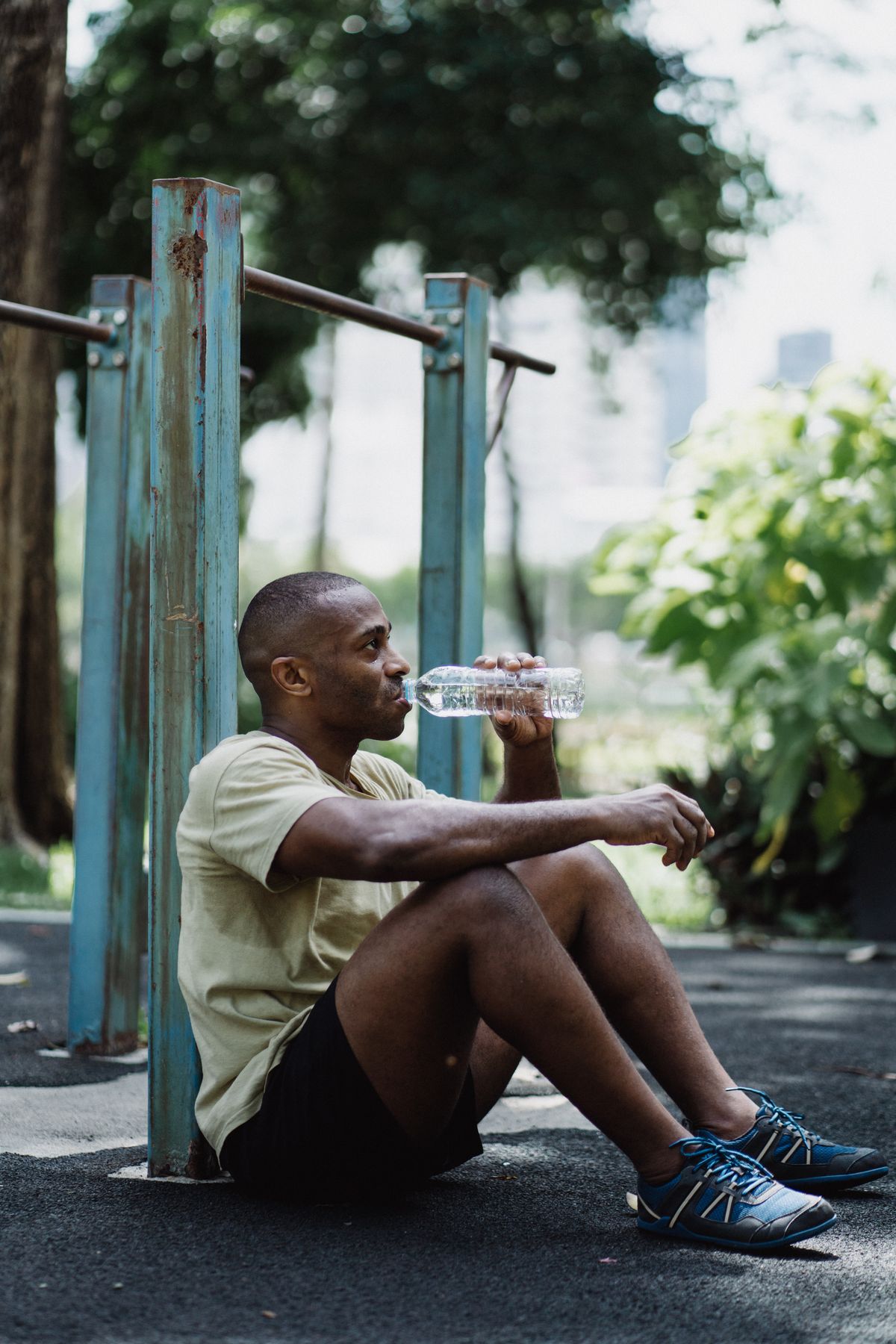 A tired man sitting on the ground in a park, drinking water after a hard run