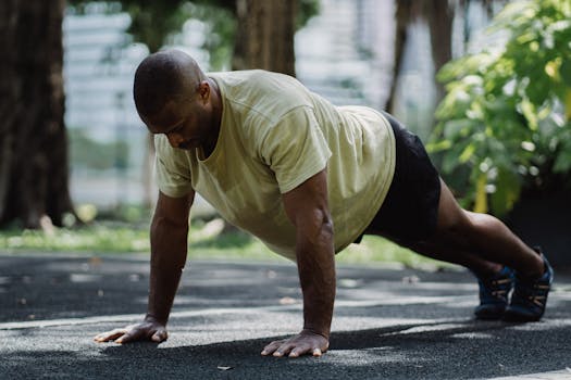 Man exercising with push-ups on pavement in summer park setting, focusing on fitness and health.