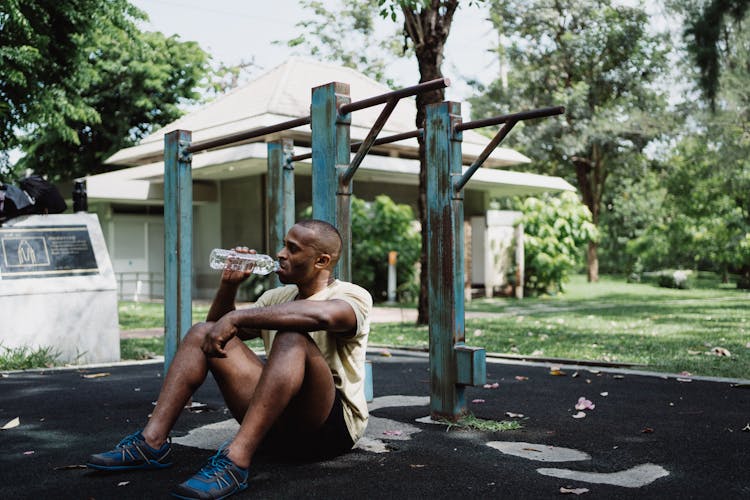 Man Sitting On Pavement While Drinking Water