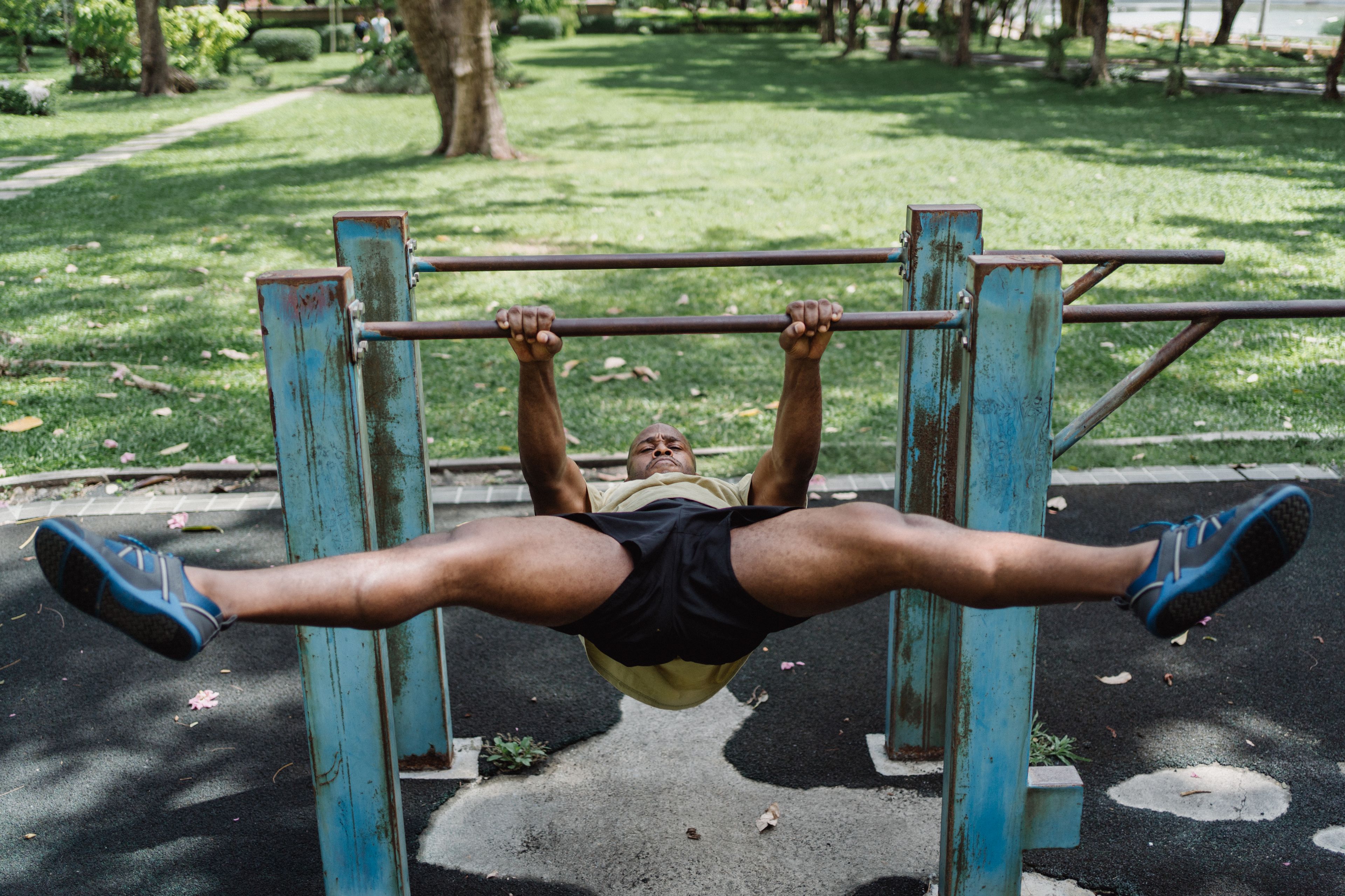 A man performing a challenging workout on parallel bars in an outdoor park setting.