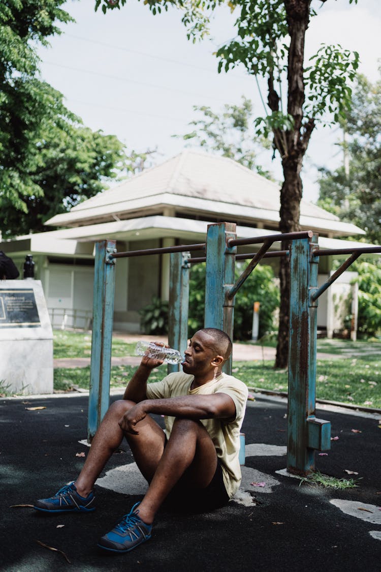 A Man Sitting On The Ground While Drinking On A Bottled Water