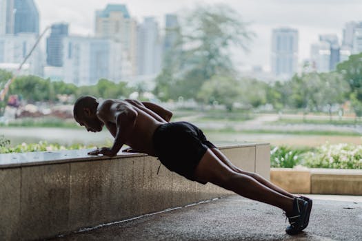 Shirtless man doing push-ups outdoors with city skyline in the background.