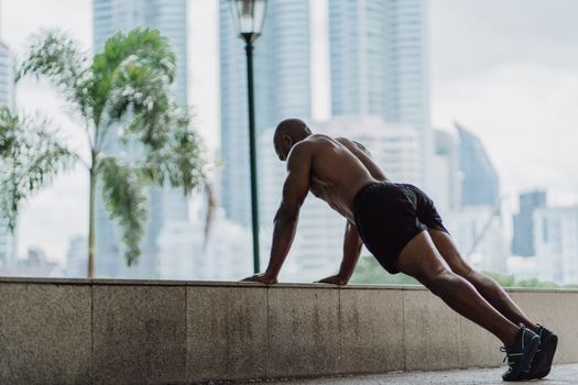 Athletic man performs push-ups on a ledge with an urban cityscape backdrop.