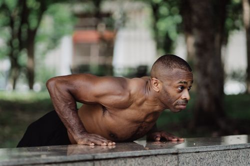 Free A muscular man performing push-ups on a concrete surface in a park, showcasing strength and fitness. Stock Photo