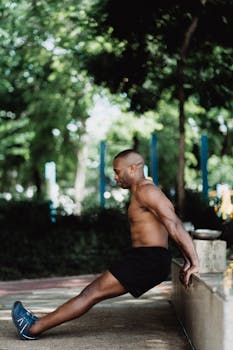 Shirtless man performing strength exercise against a concrete wall outdoors.