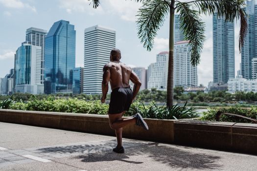 Shirtless man jogging in city park with skyscrapers in the background. Fitness and urban lifestyle concept.
