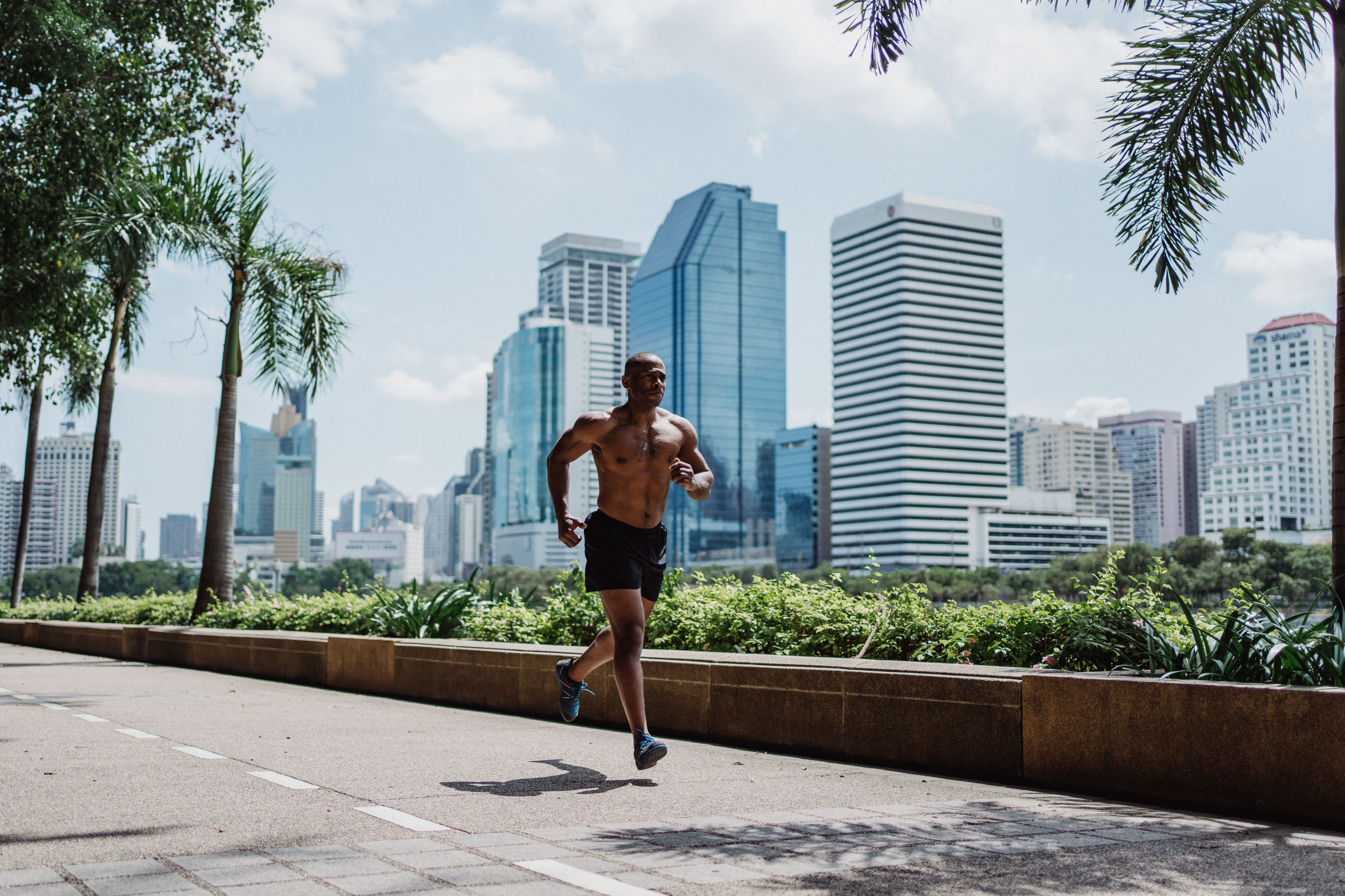 A fit man jogging on a city path framed by skyscrapers and palm trees, embodying urban fitness.