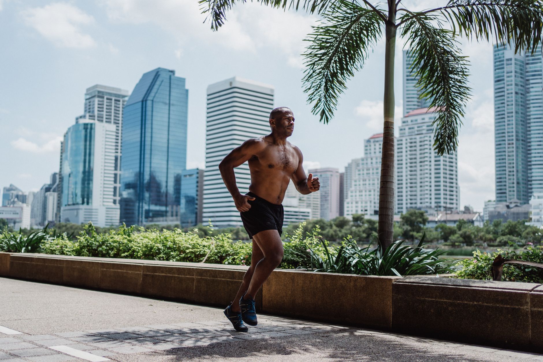 TRT benefits — A muscular man jogging in an urban park with a city skyline in the background.