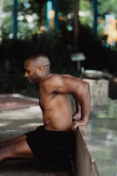 Shirtless man performs tricep dips outside, showcasing strength and fitness.