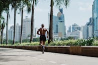 阳光明媚的日子里，一名赤裸上身的男子在高楼林立的城市中慢跑