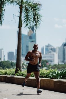 A fit man jogging outdoors on a sunny day with skyscrapers in the background.