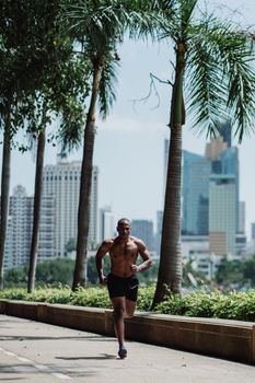 African American man jogging through a park amidst tall buildings and palm trees, representing urban fitness.