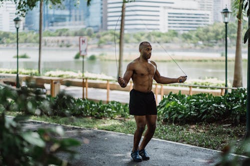 Free Topless Man Holding a Jumping Rope on Walkway of a Park  Beside the Lake Stock Photo