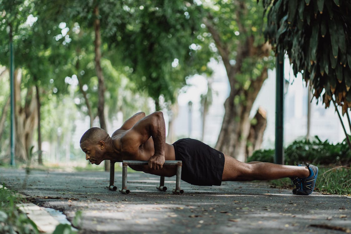 Free Shirtless Man in Black Shorts Doing PushUps on Low Dip Bars in the Park Stock Photo