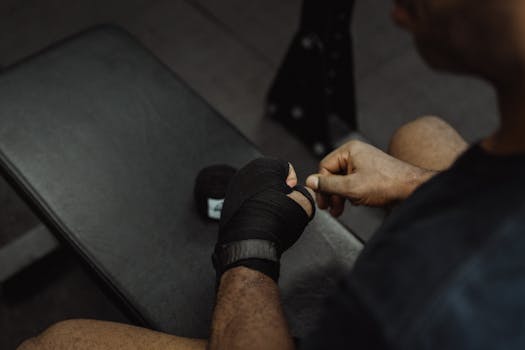 Athlete wrapping hands with black boxing tape in a gym setting, preparing for a workout.