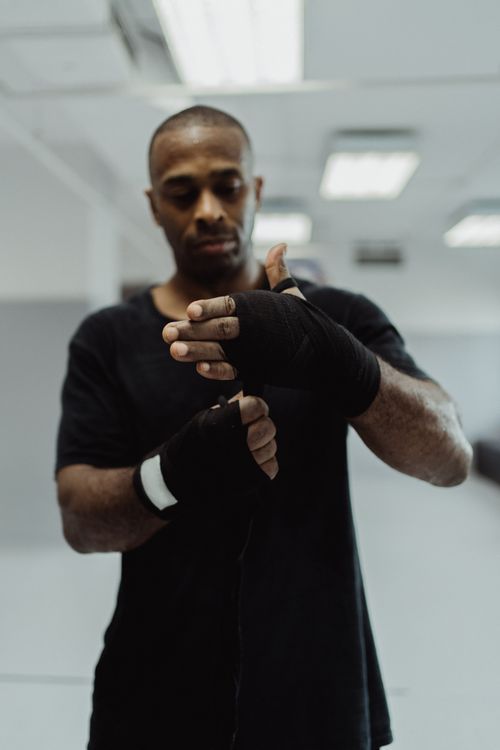 Free African American man wearing black wraps on his hands for boxing preparation in a gym setting. Stock Photo