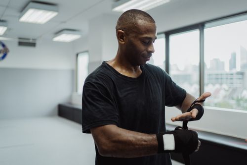 Free Serious African American man in black shirt wrapping hands in gym setting. Stock Photo