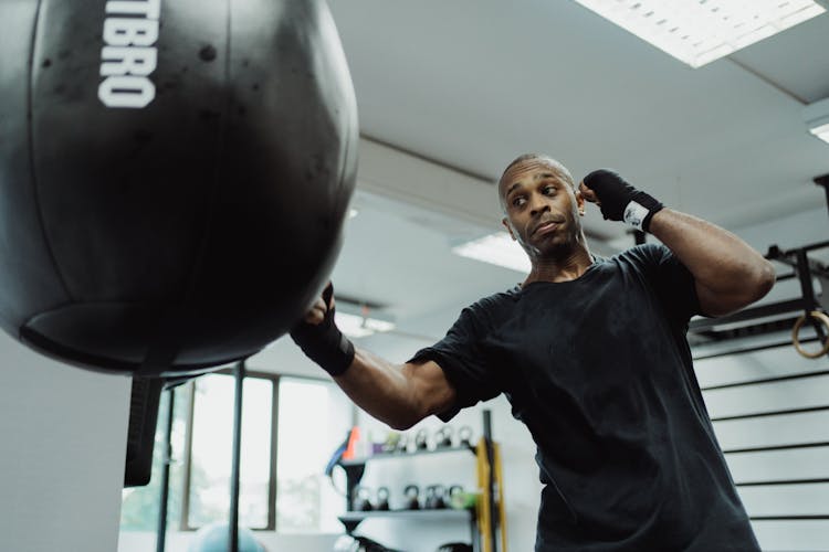 A Man With Bandages On His Hand Hitting A Punching Bag