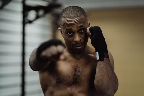 Free African American male boxer in a gym, ready to strike, showcasing strength and focus. Stock Photo