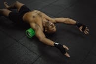 Shirtless man exercising with a foam roller in a fitness center.