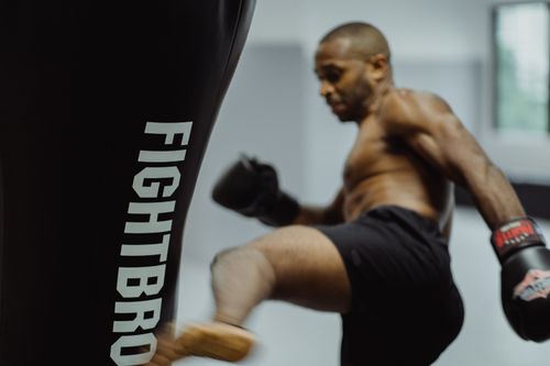 Free Athletic man practicing kicks with boxing gloves and punching bag indoors. Stock Photo