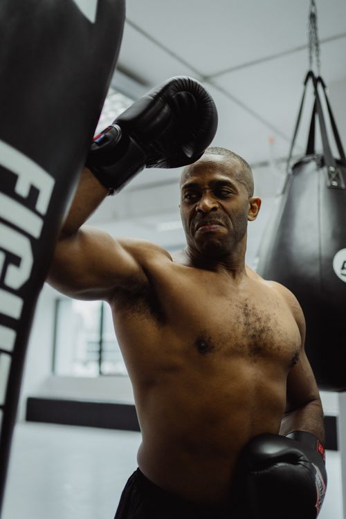 Free Determined boxer training indoors with punching bags, showcasing strength and focus. Stock Photo