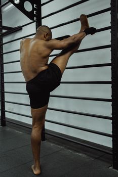 Bare-chested man in gym performing dynamic stretches on metal bars, showcasing flexibility and strength.
