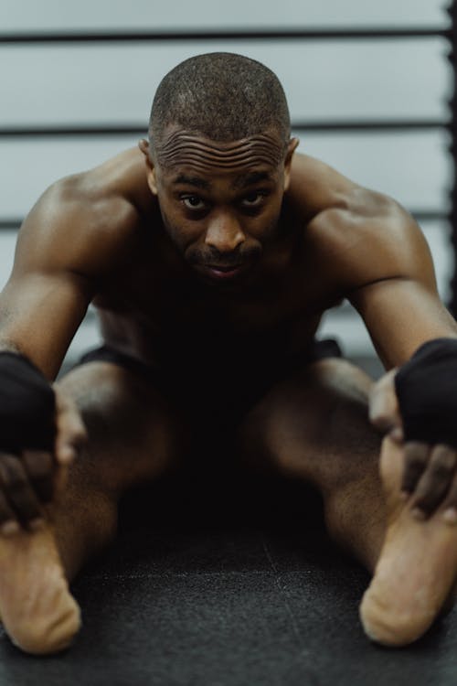 Free Shirtless Man Holding His Feet While Sitting on the Floor  Stock Photo