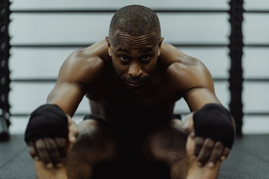 Topless African American man with hand wraps stretching in a gym environment.