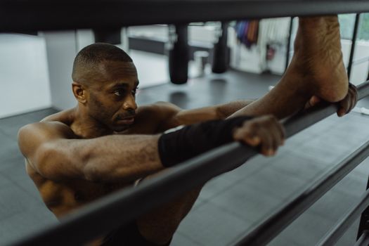 Focused African American man stretching and warming up on stall bars in a gym setting.